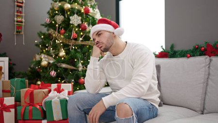 Photo for Young hispanic man wearing christmas hat looking upset at home - Royalty Free Image
