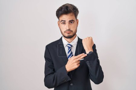 Photo for Young hispanic man with tattoos wearing business suit and tie in hurry pointing to watch time, impatience, looking at the camera with relaxed expression - Royalty Free Image