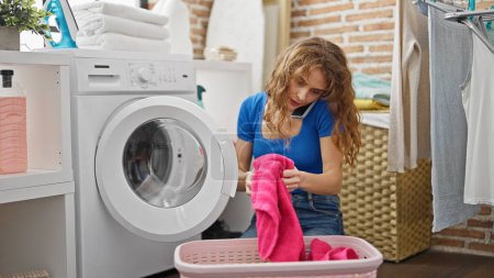 Téléchargez les photos : Jeune femme laver des vêtements parler sur smartphone à la buanderie - en image libre de droit