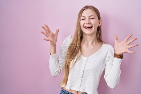 Photo for Young caucasian woman standing over pink background celebrating mad and crazy for success with arms raised and closed eyes screaming excited. winner concept - Royalty Free Image