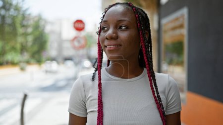 Téléchargez les photos : Femme afro-américaine confiante, souriante radieuse, regardant vers le côté dans une rue ensoleillée de la ville, exsudant positivité et joie - en image libre de droit