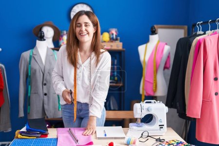 Téléchargez les photos : Jeune femme tailleur souriant tissu de coupe confiant au studio de couture - en image libre de droit