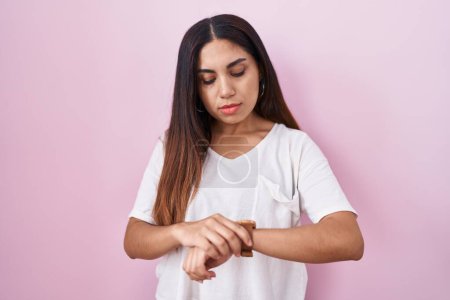 Photo for Young arab woman standing over pink background checking the time on wrist watch, relaxed and confident - Royalty Free Image