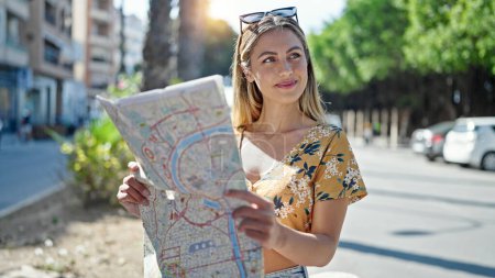 Téléchargez les photos : Jeune femme blonde touriste souriant confiant regarder la carte de la ville à la rue - en image libre de droit