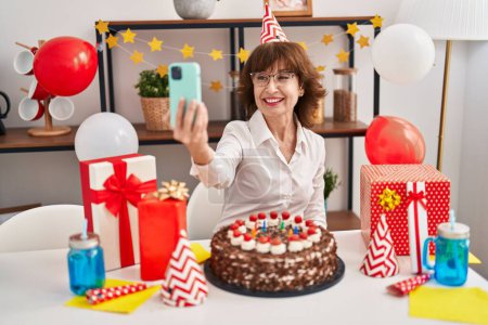 Photo for Middle age woman celebrating birthday make selfie by smartphone at home - Royalty Free Image