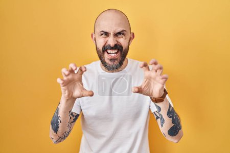 Photo for Young hispanic man with tattoos standing over yellow background smiling funny doing claw gesture as cat, aggressive and sexy expression - Royalty Free Image