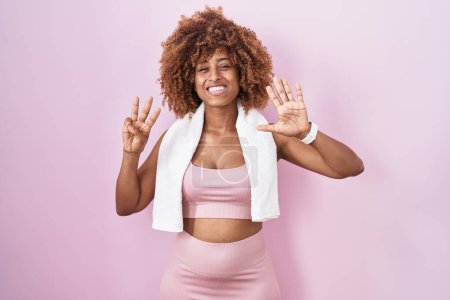 Photo for Young hispanic woman with curly hair wearing sportswear and towel showing and pointing up with fingers number eight while smiling confident and happy. - Royalty Free Image