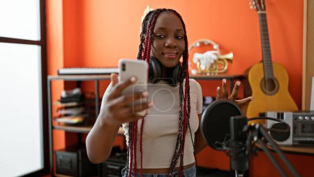 Photo for Beautiful african american woman, adult musician wearing headphones, in music studio for a lively video call conversation - authentic portrait of a professional artist indoors - Royalty Free Image