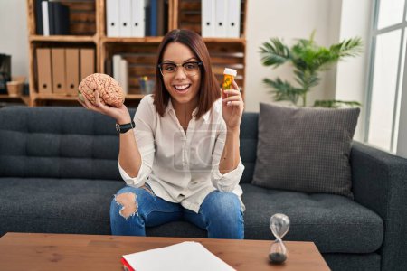 Photo for Young hispanic woman working on depression holding pills smiling and laughing hard out loud because funny crazy joke. - Royalty Free Image