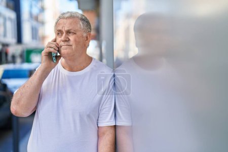 Téléchargez les photos : Moyen-âge homme aux cheveux gris parler sur smartphone avec une expression détendue à la rue - en image libre de droit