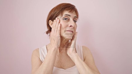 Téléchargez les photos : Femme hispanique mature regardant sérieusement toucher le visage avec la main sur fond rose isolé - en image libre de droit