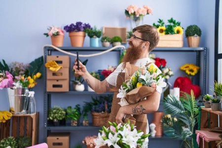 Foto de Joven florista pelirroja hombre hacer selfie por teléfono inteligente celebración de flores en la tienda de flores - Imagen libre de derechos