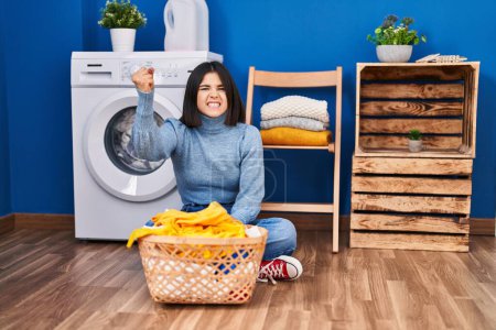 Photo for Young hispanic woman at laundry room annoyed and frustrated shouting with anger, yelling crazy with anger and hand raised - Royalty Free Image