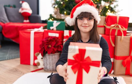 Téléchargez les photos : Adorable fille hispanique tenant cadeau de Noël assis sur le sol à la maison - en image libre de droit