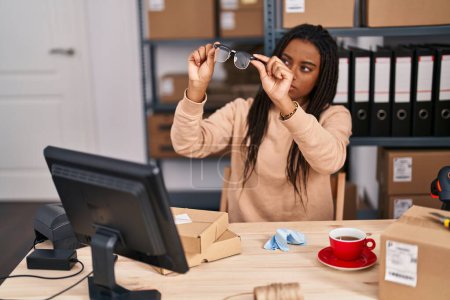 Téléchargez les photos : Africaine américaine femme commerce électronique travailleur d'affaires à la recherche de lunettes propres au bureau - en image libre de droit