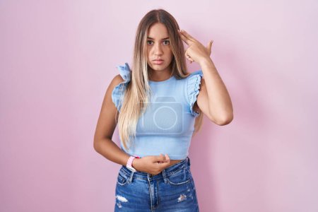 Photo for Young blonde woman standing over pink background shooting and killing oneself pointing hand and fingers to head like gun, suicide gesture. - Royalty Free Image