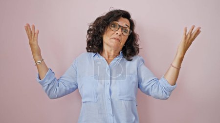 Foto de Mujer hispana de mediana edad de pie despistada sobre un fondo rosa aislado - Imagen libre de derechos