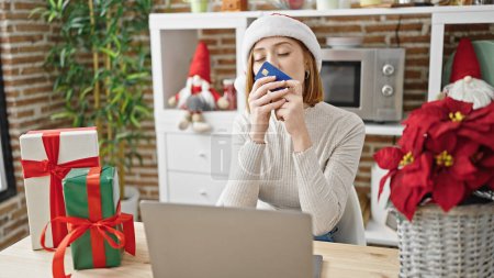 Téléchargez les photos : Jeune femme blonde faisant du shopping avec ordinateur portable et carte de crédit célébrant Noël à la salle à manger - en image libre de droit