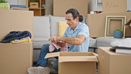 Photo for Middle age man unpacking cardboard box at new home - Royalty Free Image