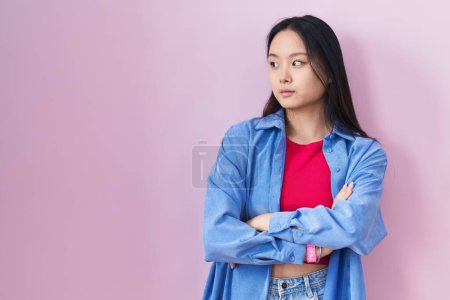 Téléchargez les photos : Jeune femme asiatique debout sur fond rose regardant sur le côté avec les bras croisés convaincu et confiant - en image libre de droit