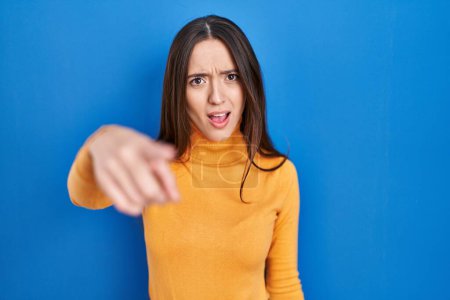 Photo for Young brunette woman standing over blue background pointing displeased and frustrated to the camera, angry and furious with you - Royalty Free Image