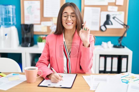 Photo for Young hispanic woman working at the office wearing glasses gesturing finger crossed smiling with hope and eyes closed. luck and superstitious concept. - Royalty Free Image