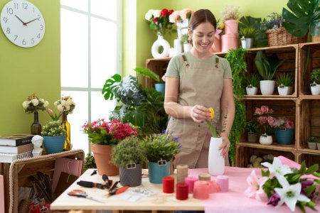 Téléchargez les photos : Jeune belle femme fleuriste souriant confiant tenant fleur à la boutique de fleurs - en image libre de droit