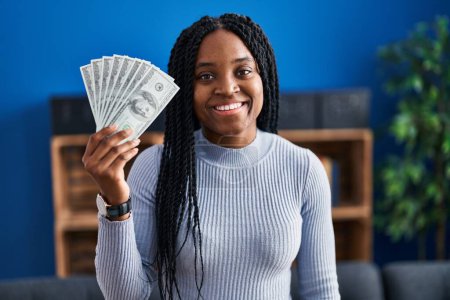 Photo for African american woman holding dollars banknotes looking positive and happy standing and smiling with a confident smile showing teeth - Royalty Free Image