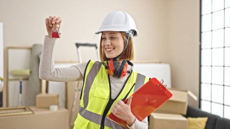 Photo for Young blonde woman architect holding keys of new home and clipboard at new home - Royalty Free Image