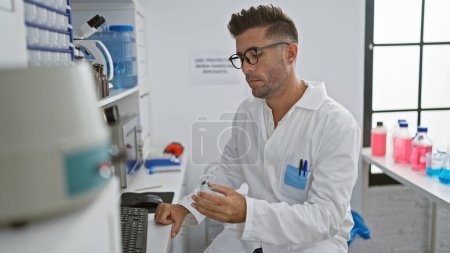 Photo for Attractive young hispanic man, working tirelessly in the lab, engrossed scientist holding a test tube, fixated on computer screens while experimenting with cutting-edge medical technology. - Royalty Free Image