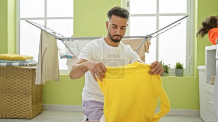 Photo for Young arab man folding clothes at laundry room - Royalty Free Image