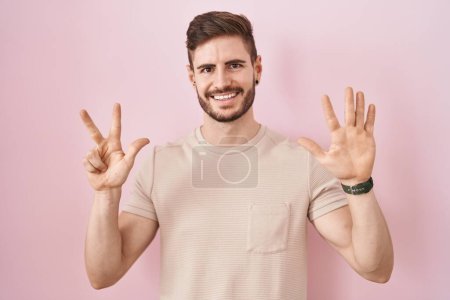 Téléchargez les photos : Homme hispanique avec barbe debout sur fond rose montrant et pointant vers le haut avec les doigts numéro huit tout en souriant confiant et heureux. - en image libre de droit