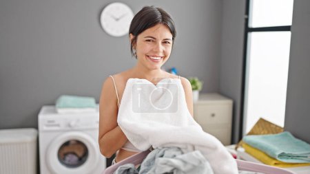 Téléchargez les photos : Jeune belle femme hispanique souriante confiante sentant les vêtements propres à la buanderie - en image libre de droit