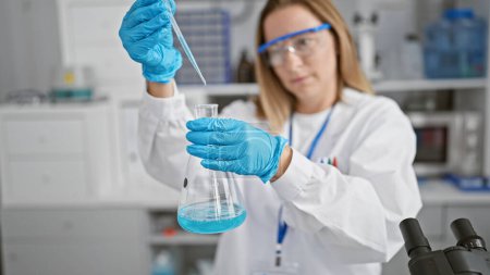 Foto de Preciosa joven científica rubia en el laboratorio, precisión en el trabajo mientras mide y vierte líquido en un tubo de ensayo para la investigación médica - Imagen libre de derechos