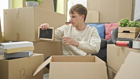 Téléchargez les photos : Young caucasian man packing cardboard box at new home - en image libre de droit