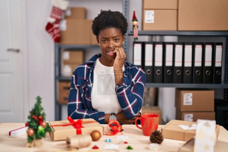 Foto de Mujer afroamericana trabajando en pequeñas empresas haciendo decoración navideña luciendo estresada y nerviosa con las manos en la boca mordiendo uñas. problema de ansiedad. - Imagen libre de derechos