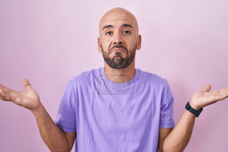 Photo for Middle age bald man standing over pink background clueless and confused expression with arms and hands raised. doubt concept. - Royalty Free Image