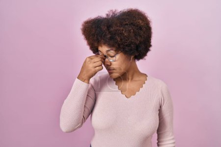 Foto de Mujer afroamericana joven de pie sobre fondo rosa cansada frotando nariz y ojos sintiendo fatiga y dolor de cabeza. concepto de estrés y frustración. - Imagen libre de derechos
