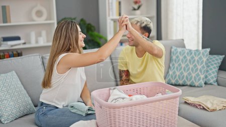 Photo for Beautiful couple folding clothes high five at home - Royalty Free Image