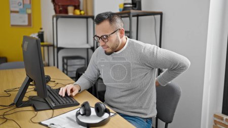 Foto de Hombre hispano trabajador de negocios sentado en la mesa sufriendo por dolor de espalda en la oficina - Imagen libre de derechos