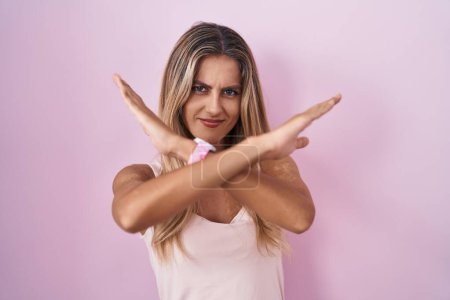 Téléchargez les photos : Young blonde woman standing over pink background rejection expression crossing arms doing negative sign, angry face - en image libre de droit