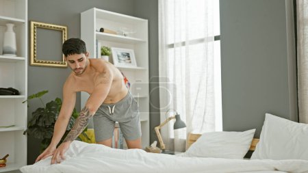 Téléchargez les photos : Jeune homme hispanique faire lit dans la chambre - en image libre de droit