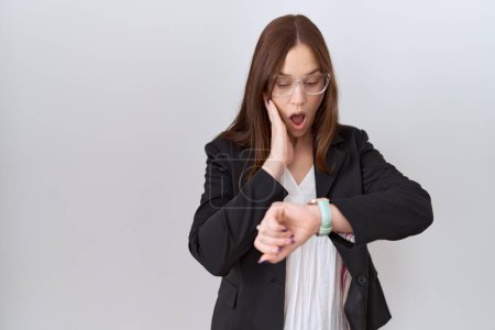 Photo for Beautiful brunette woman wearing business jacket and glasses looking at the watch time worried, afraid of getting late - Royalty Free Image