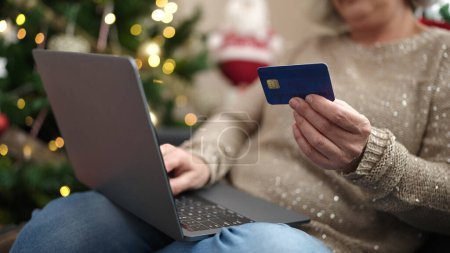 Téléchargez les photos : Femme d'âge moyen avec les cheveux gris faire des achats en ligne de Noël avec ordinateur portable à la maison - en image libre de droit