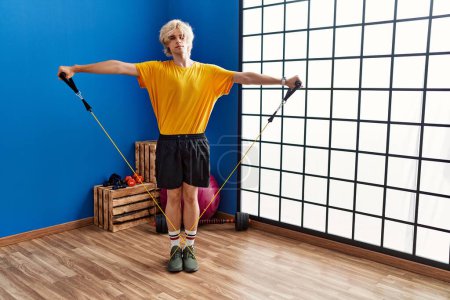Photo for Young blond man smiling confident using elastic band training at sport center - Royalty Free Image