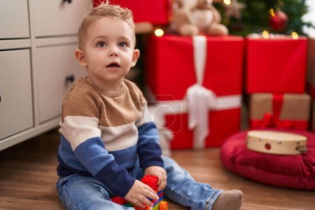 Foto de Adorable niño jugando con bloques de construcción sentado en el suelo por regalos de Navidad en casa - Imagen libre de derechos