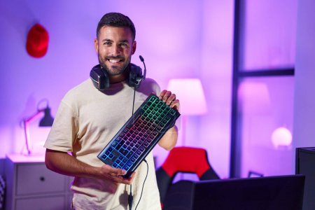 Photo for Young hispanic man streamer smiling confident holding keyboard computer at gaming room - Royalty Free Image