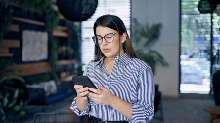 Photo for Young beautiful hispanic woman using smartphone with serious face at the office - Royalty Free Image