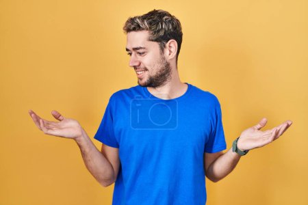 Téléchargez les photos : Homme hispanique avec barbe debout sur fond jaune souriant montrant les paumes ouvertes des deux mains, présentant et comparant la publicité et l'équilibre - en image libre de droit