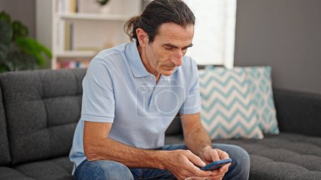 Téléchargez les photos : Middle age man using smartphone sitting on sofa at home - en image libre de droit